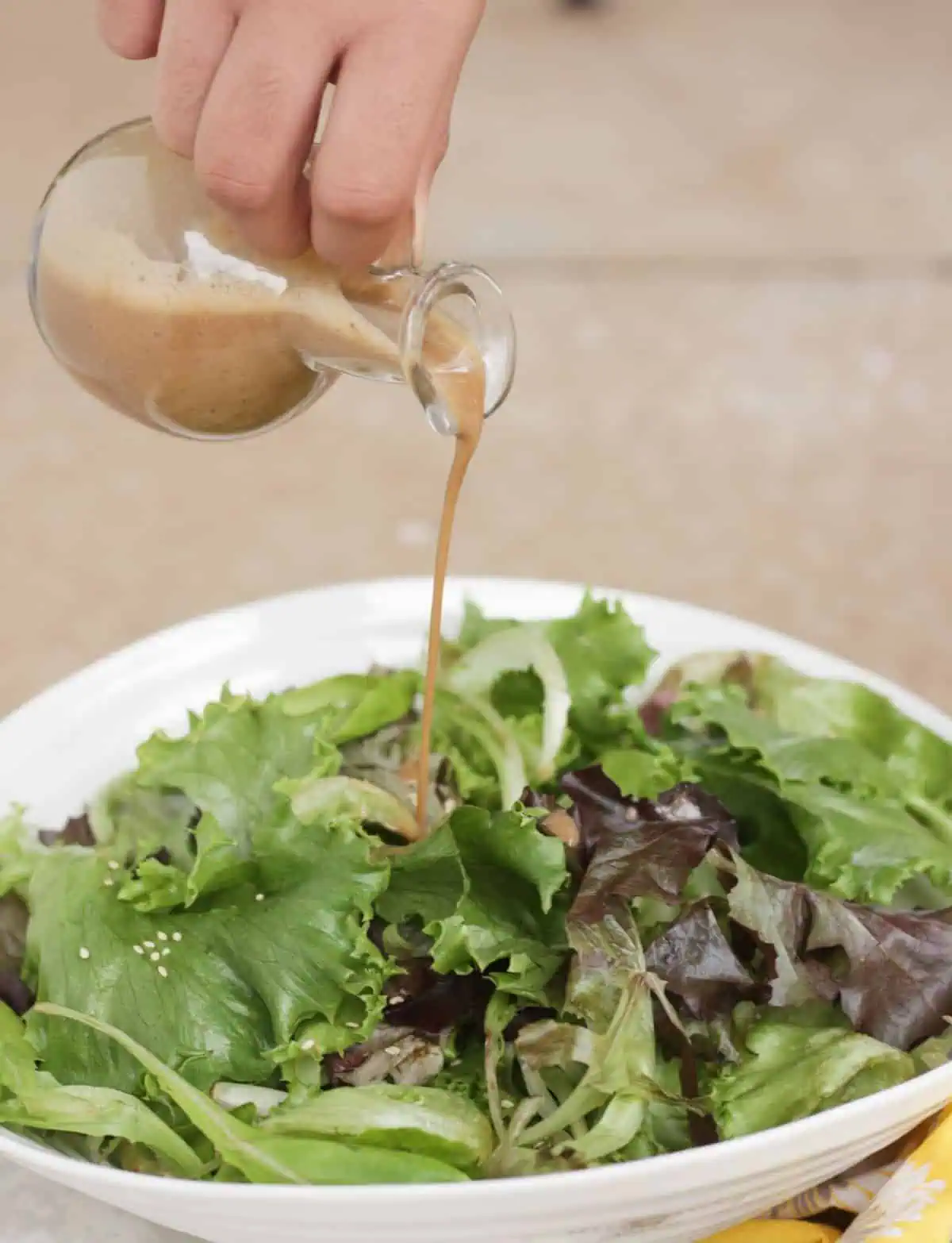 Pouting miso salad dressing onto a bowl of salad greens.