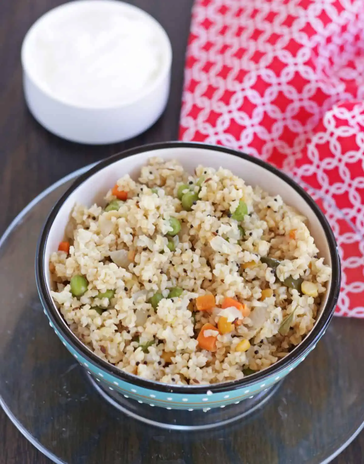 Godhumai rava upma in a bowl with yogurt in the background. 