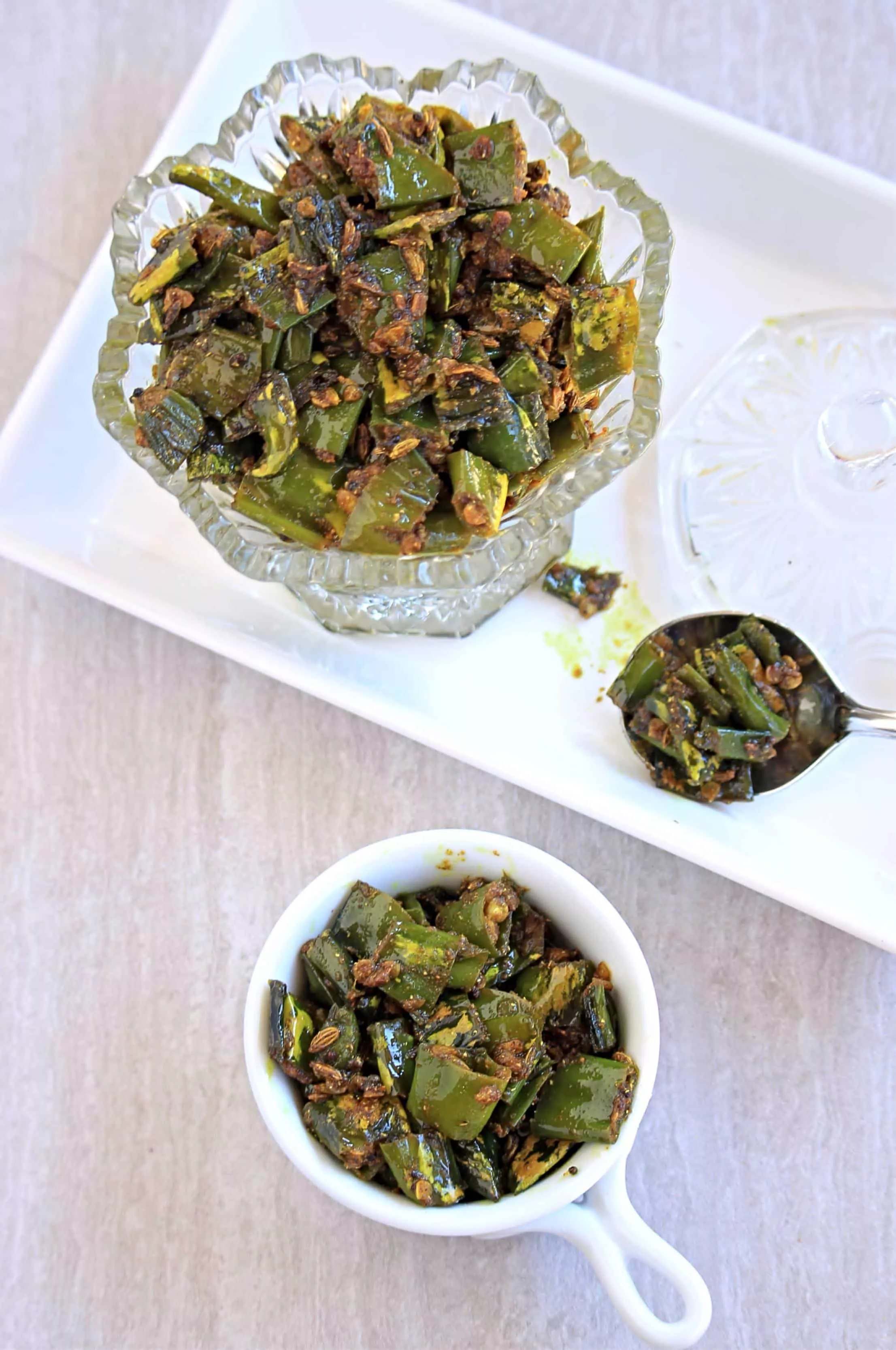 Tipore - Green chili pickle in glass container, spoon and a white bowl