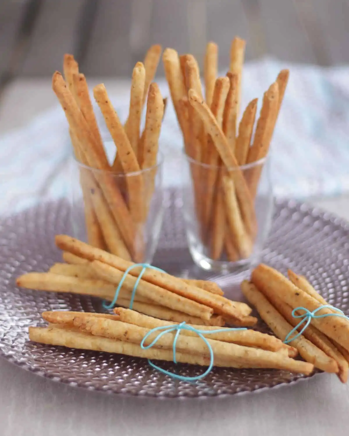 Cheese straws bundled in a plate and in two glasses. 