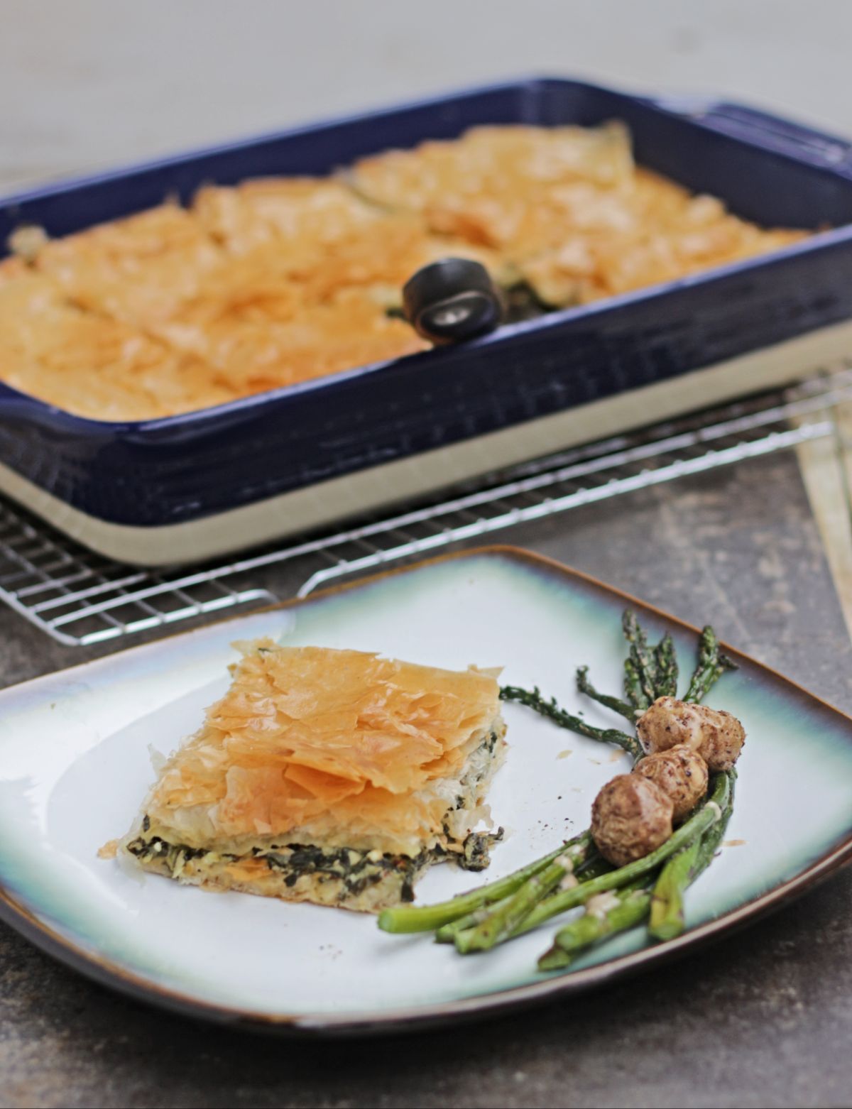 slice of spinach pie in a plate with asparagus and potato and tray in the background