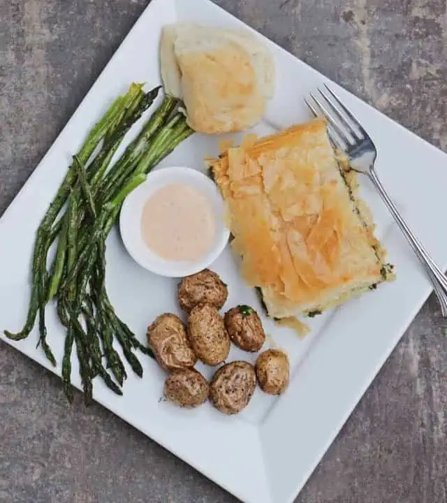 dinner plate with albanian spinach pie, roasted potatoes, asparagus, sauce and roll