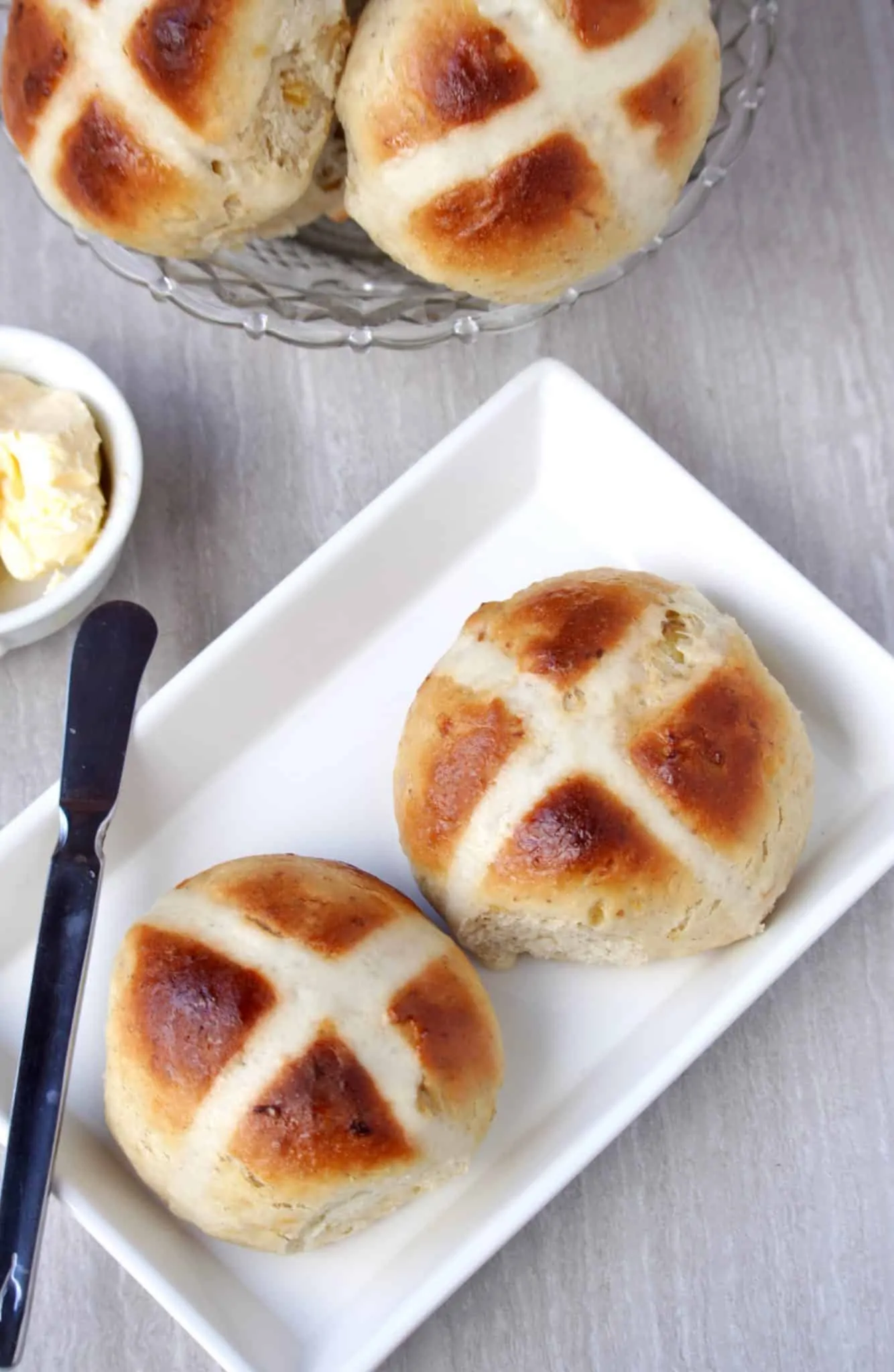 Hot Cross Buns in a white plate with butter on the side.