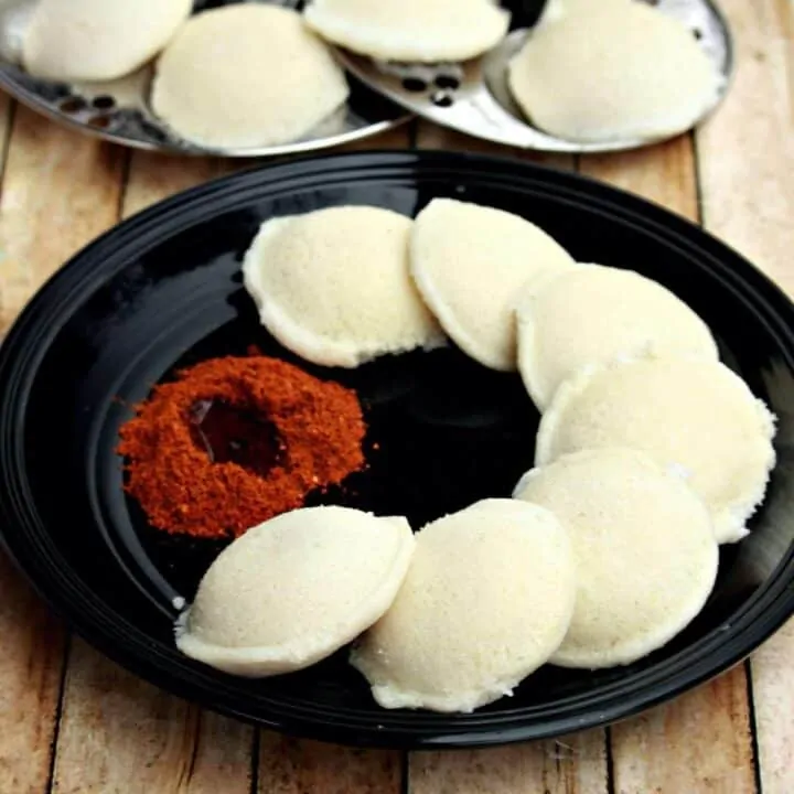 Idli in a balck plate with podi