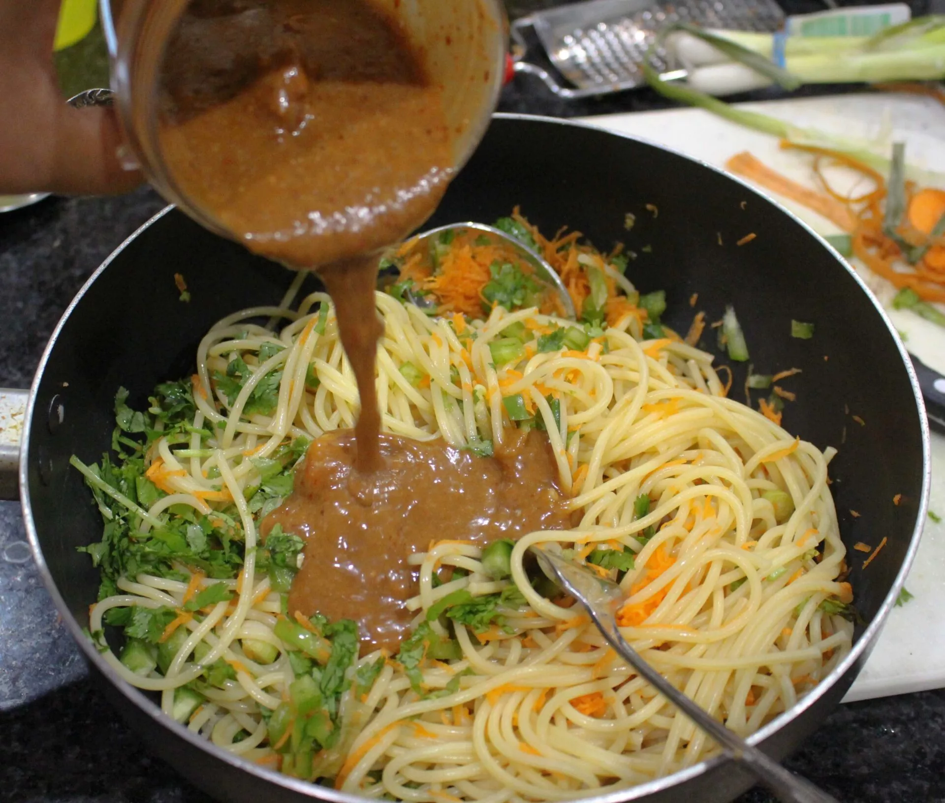 Pouring spicy peanut dressing over pasta salad