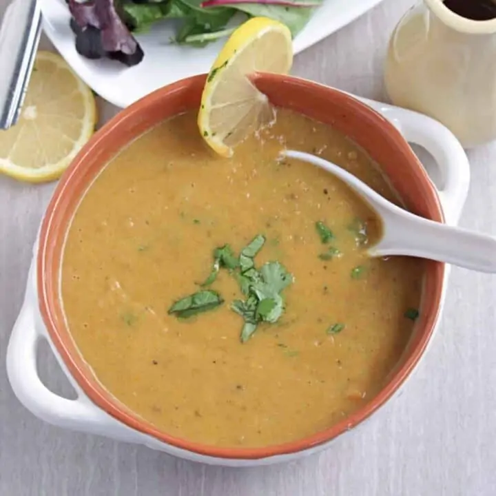 lentil soup in a bowl with a lemon piece on side and garnished with cilantro