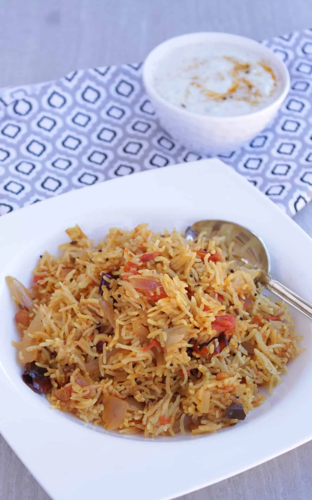 Tomato rice in a white bowl served with cucumber raita