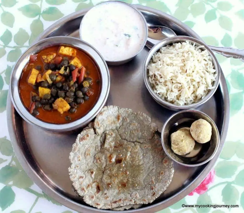 Jeera rice, subzi, raita and roti in a plate