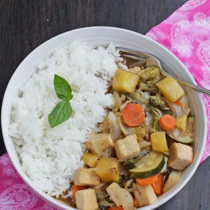 sweet and sour stir fry with vegetables and tofu served with rice in a white bowl