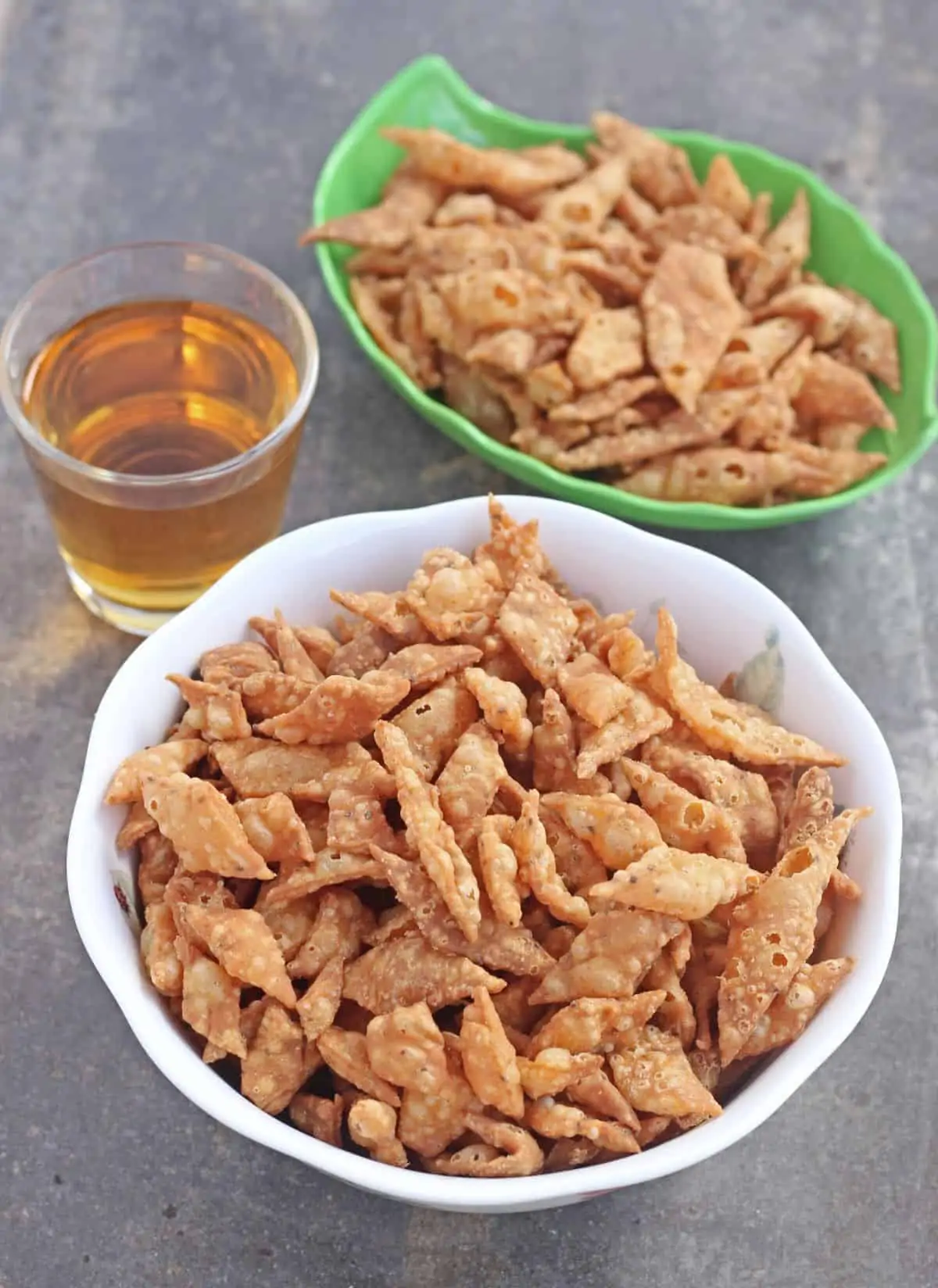 diamond shaped savory snack in a white bowl and a green bowl with apple juice on side