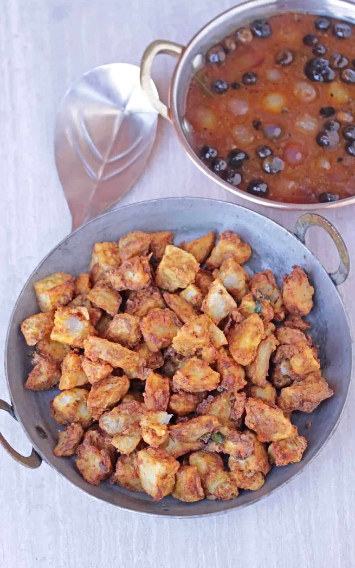 seppankizhangu roast in a pan with a ladle and vatha kuzhambu in background