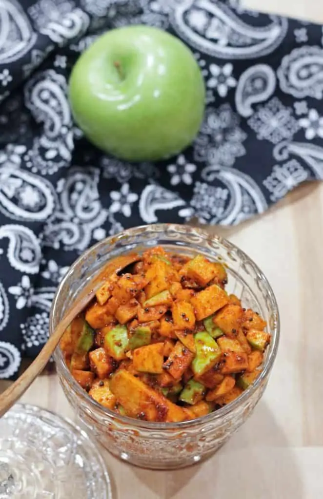 apple pickle in a jar with a spoon and a apple in the background