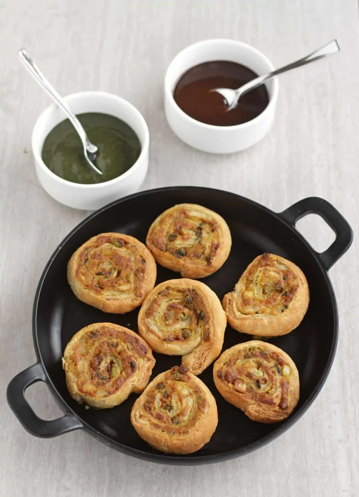 pinwheel samosa in a black plate with chutney on the side