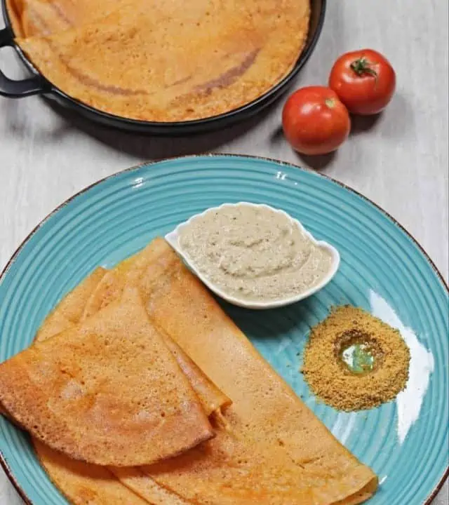 tomato dosa with chutney on a blue plate and black plate with tomatoes on side