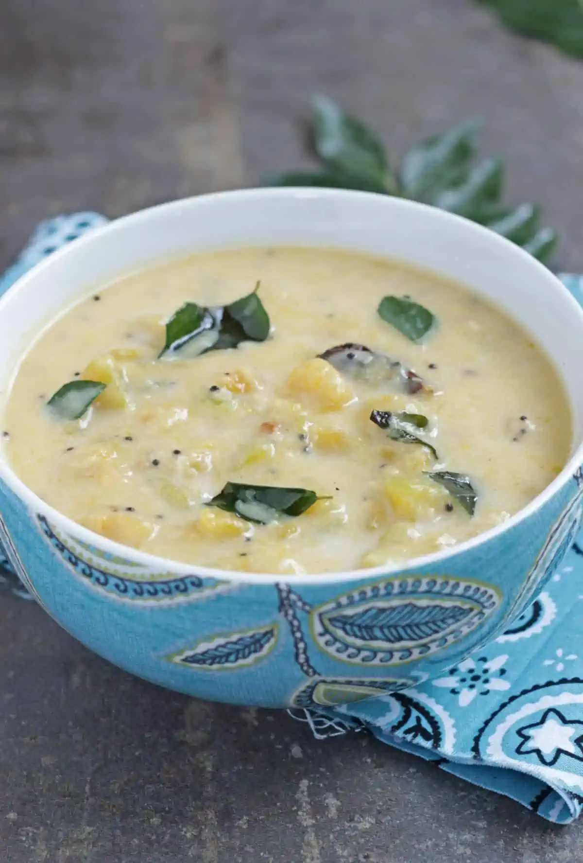 side view of kootu in a blue bowl with curry leaves on top.