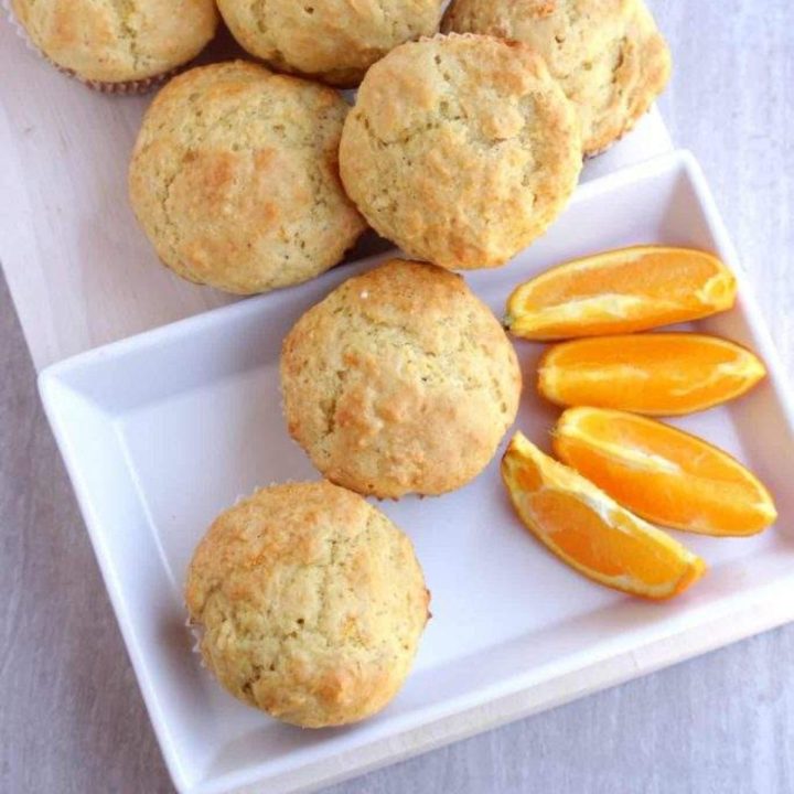 Orange muffins in a white plate with orange wedges on the side - Featured Image