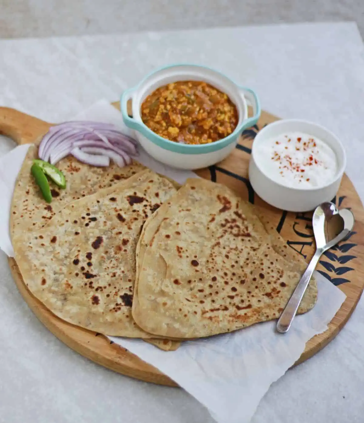 Carom Seeds Paratha along with subzi and yogurt and sliced onion and green chilies on a plate.