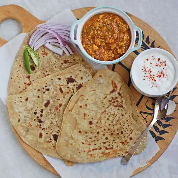 a lunch platter with paratha, subzi and yogurt along with salad.